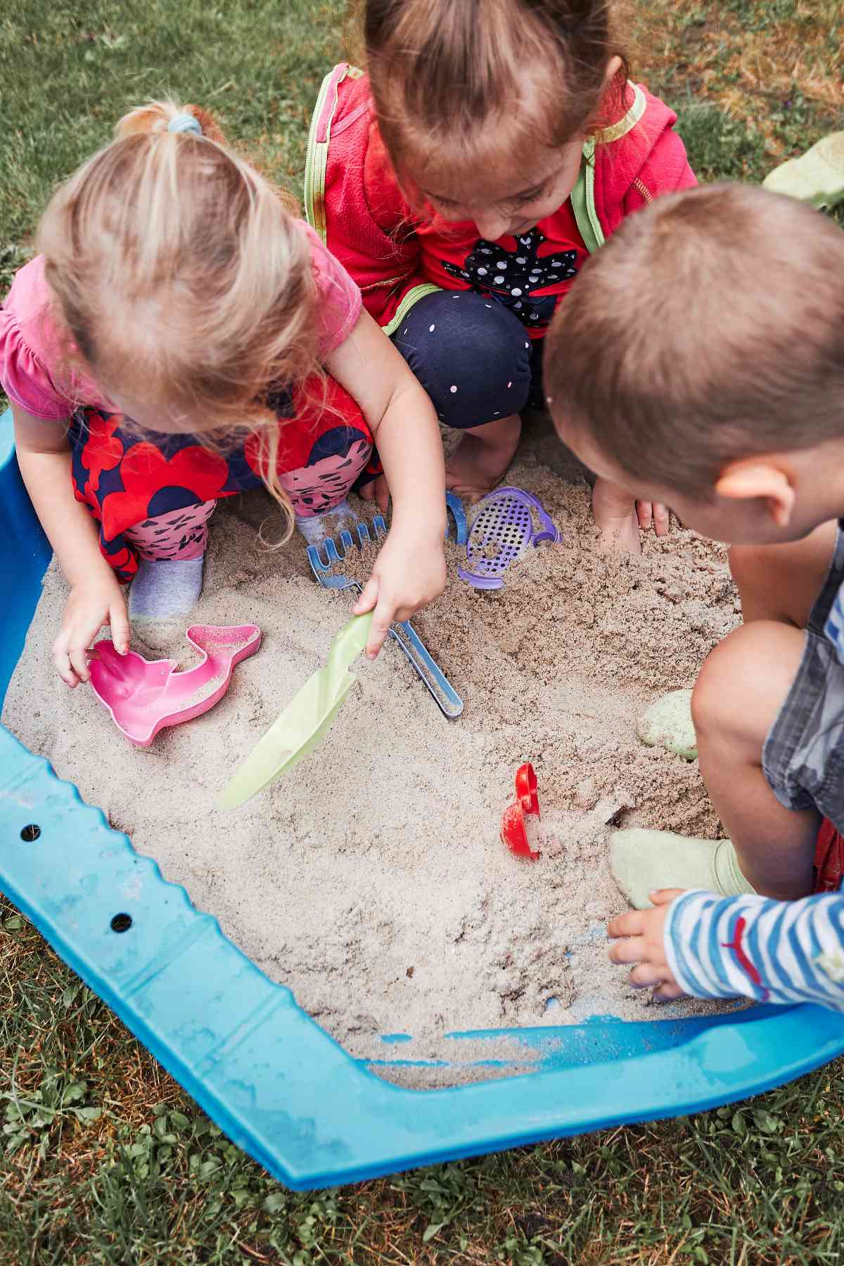 Three children playing together in a sandbox with toys.