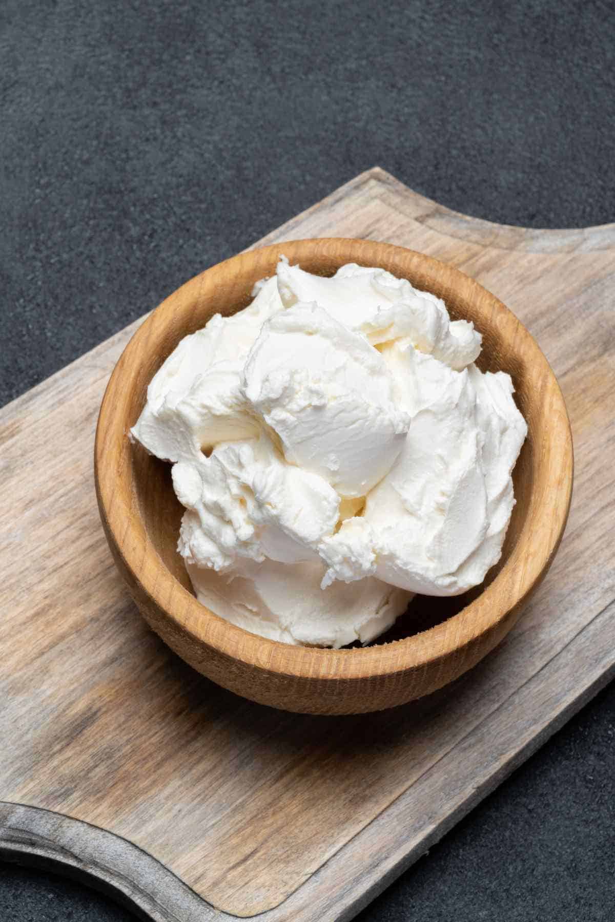 A bowl of mascarpone cheese on a wooden cutting board.