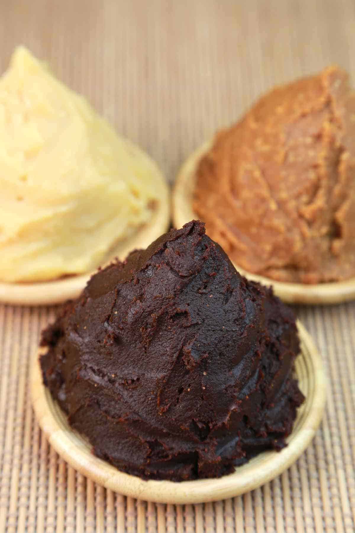 Three different types of traditional miso paste displayed in small wooden bowls.
