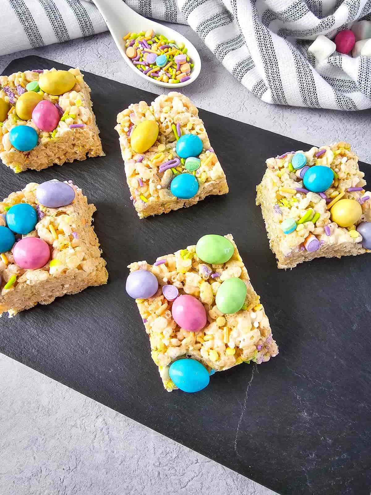M&M rice krispie treats topped with colorful peanut M&Ms and sprinkles on a serving board.