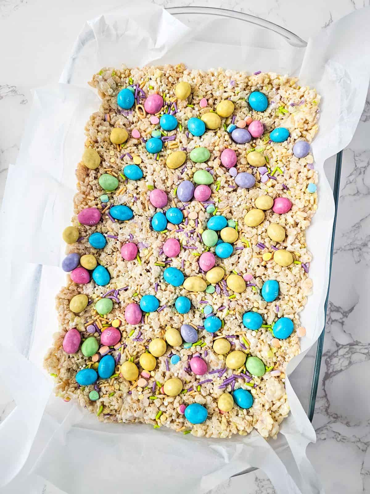 A tray of rice cereal treat with colorful M&M candy toppings on a marble surface.