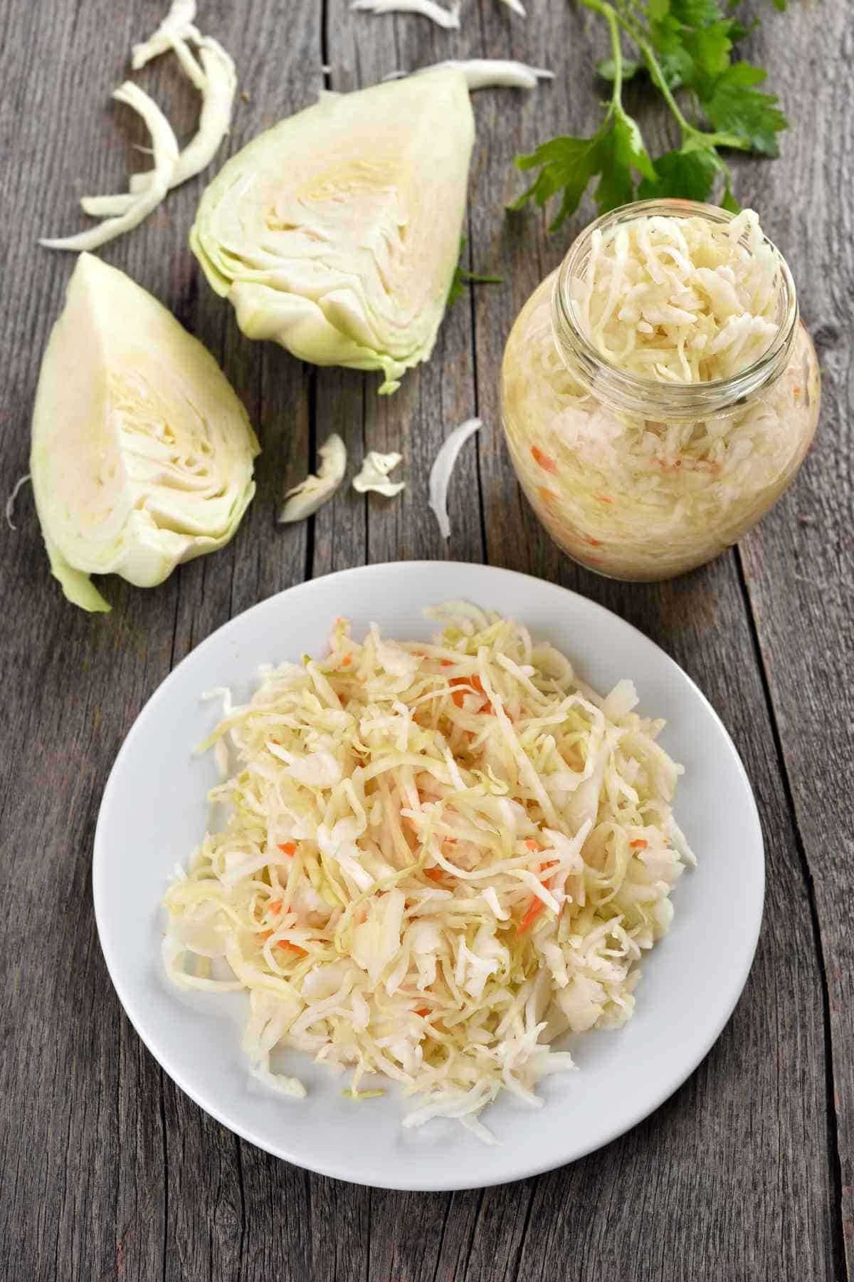 A plate and a jar of sauerkraut with sliced cabbage on a wooden table.