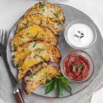 A plate of air fryer eggplant slices topped with melted cheese and garnished with chopped herbs, served on a white plate.