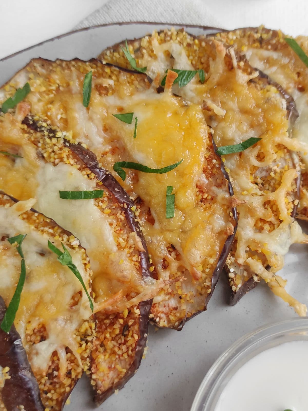 Air fryer eggplant slices topped with melted cheese and garnished with chopped herbs, served on a white plate.