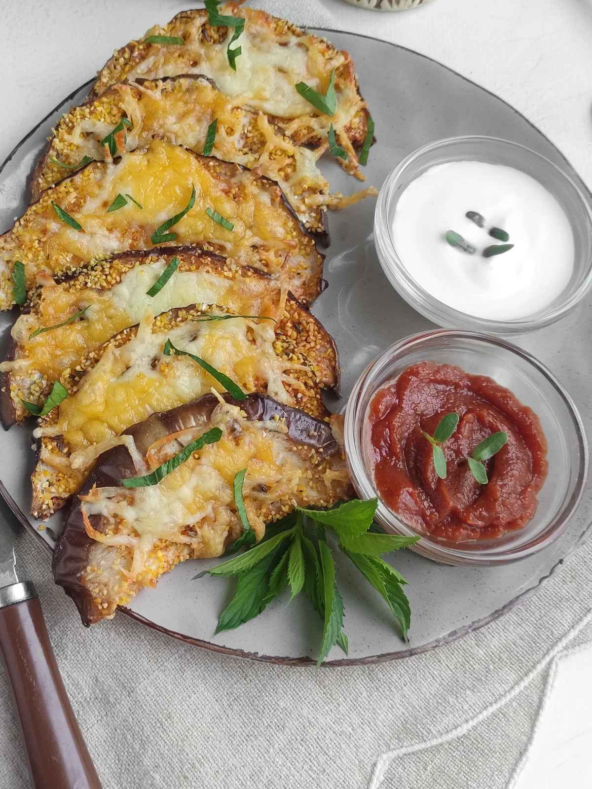 A plate of air fryer eggplant slices topped with melted cheese and garnished with chopped herbs, served on a white plate.