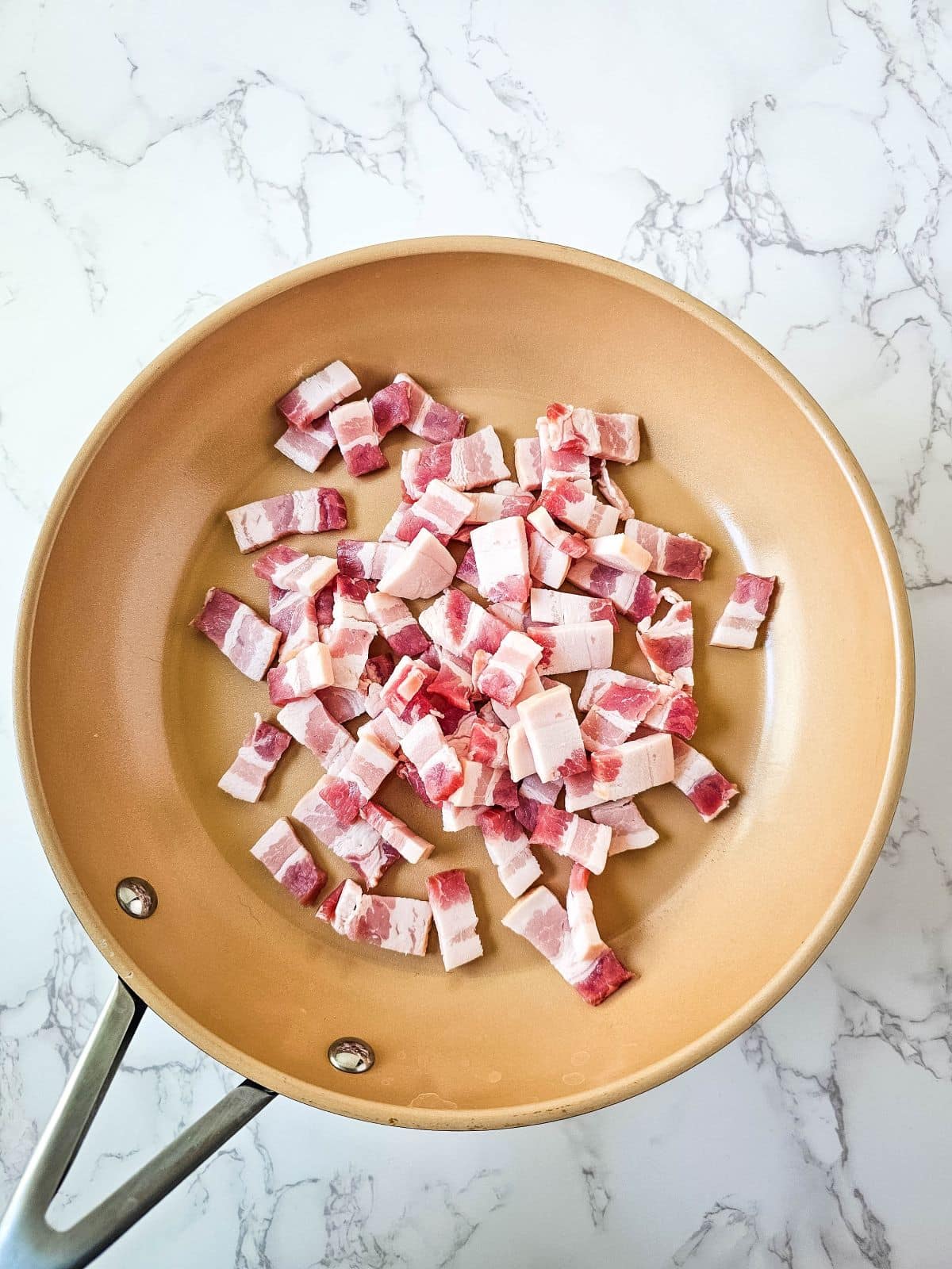 Diced raw pork bacon in a large pan on a marble countertop.