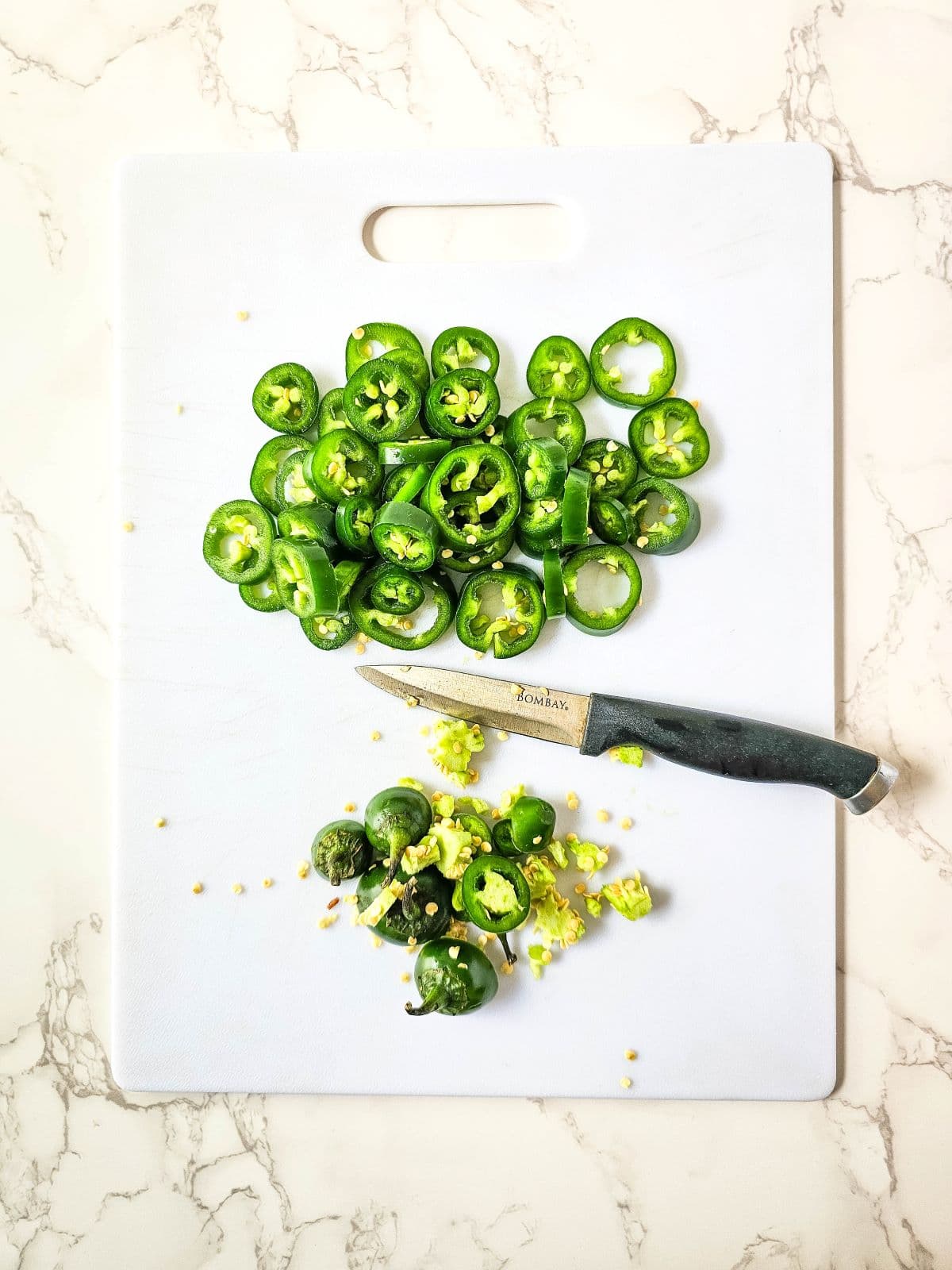 Sliced green jalapeño peppers on a white cutting board with a knife.