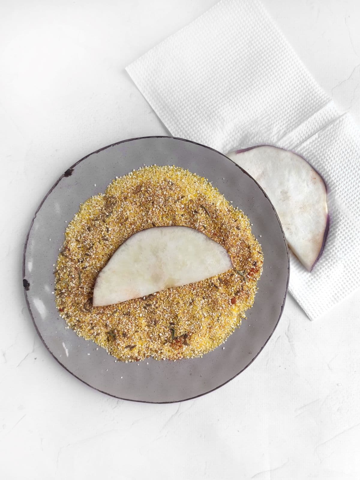 Coating an eggplant slice with corn grits and seasoning mixture.
