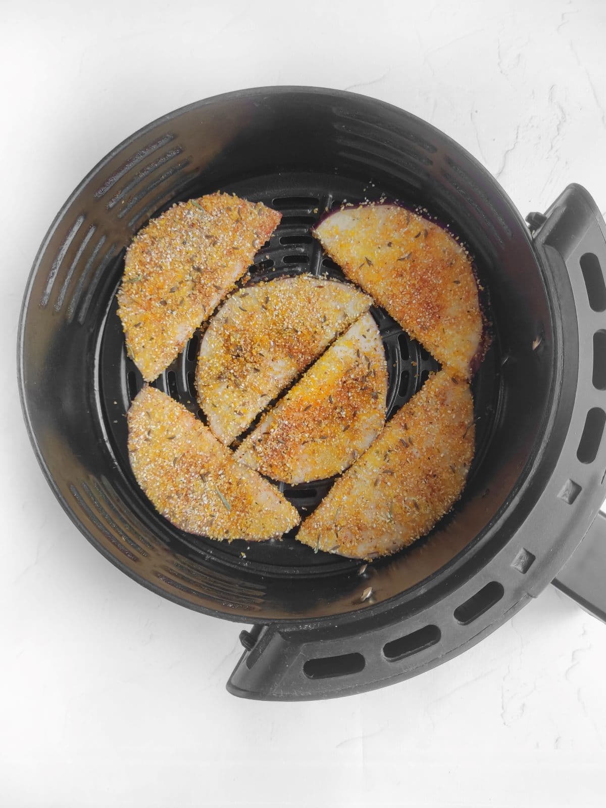 Breaded eggplant slices arranged in a black air fryer basket.