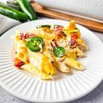 A plate of baked jalapeño poppers chicken casserole topped with bacon bits and sliced jalapeños.