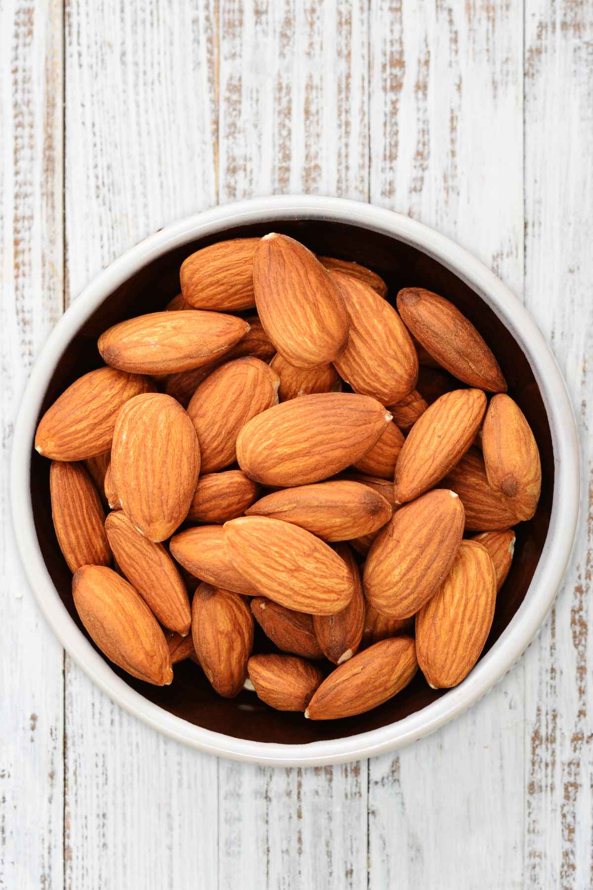 A white bowl filled with whole almonds.
