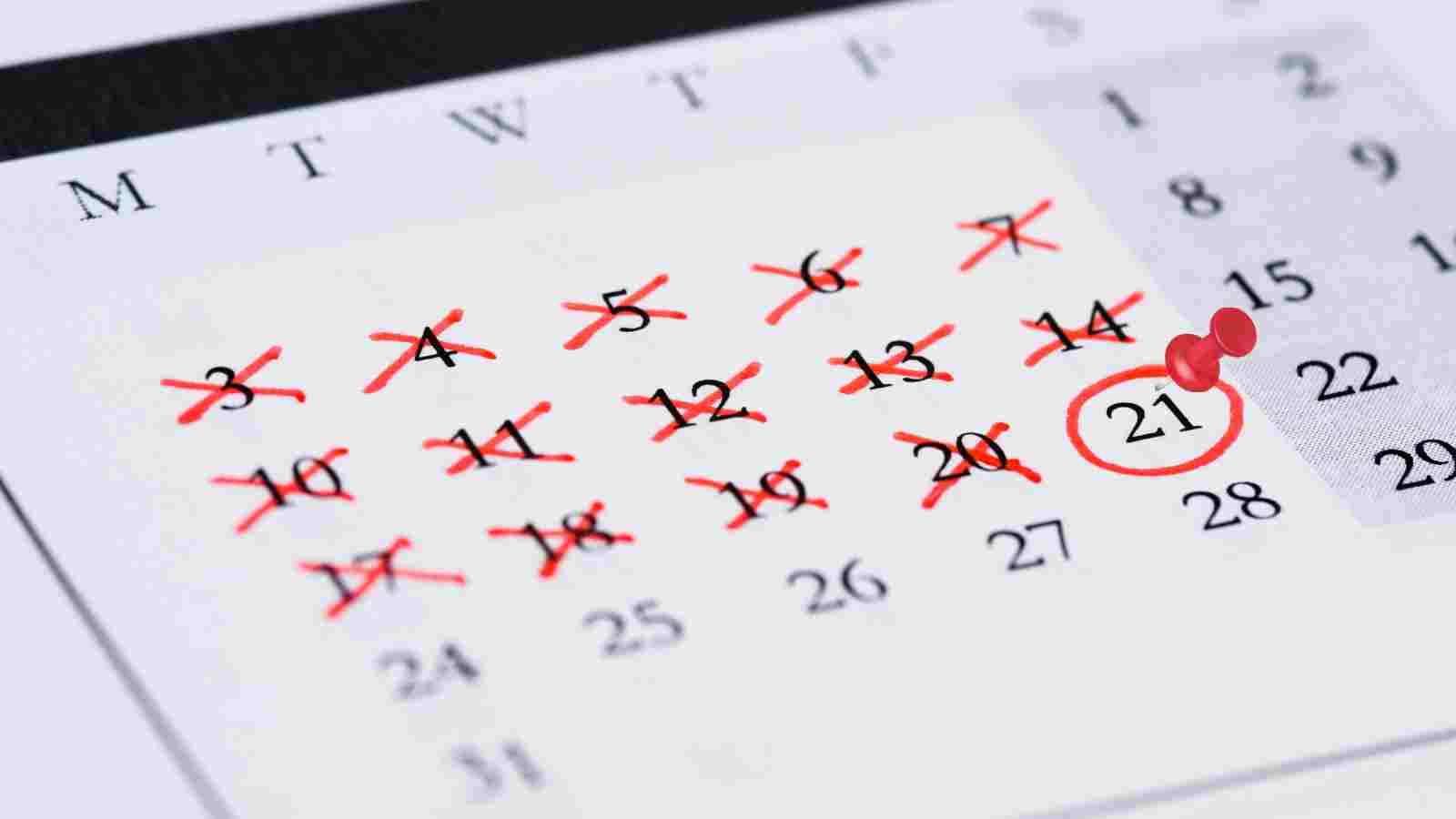 A close-up of a calendar with days from the 3rd to 20th crossed out in red. The 21st is circled with a red pin in the middle.