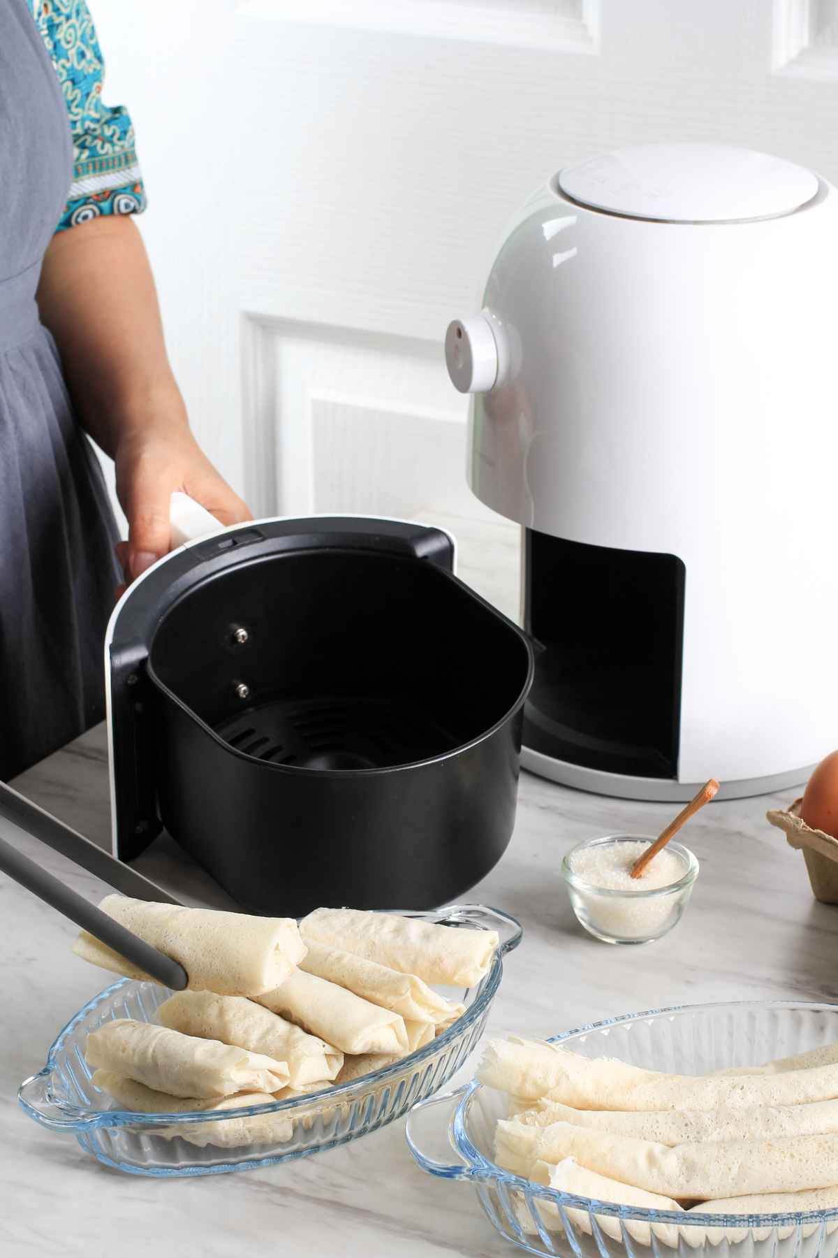 A person holding an air fryer basket near an air fryer.