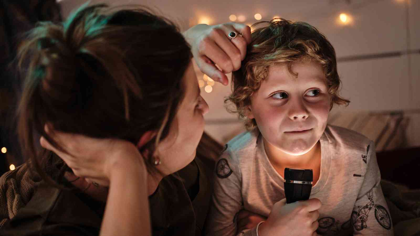 A person holds their forehead while a child next to them grips a flashlight.