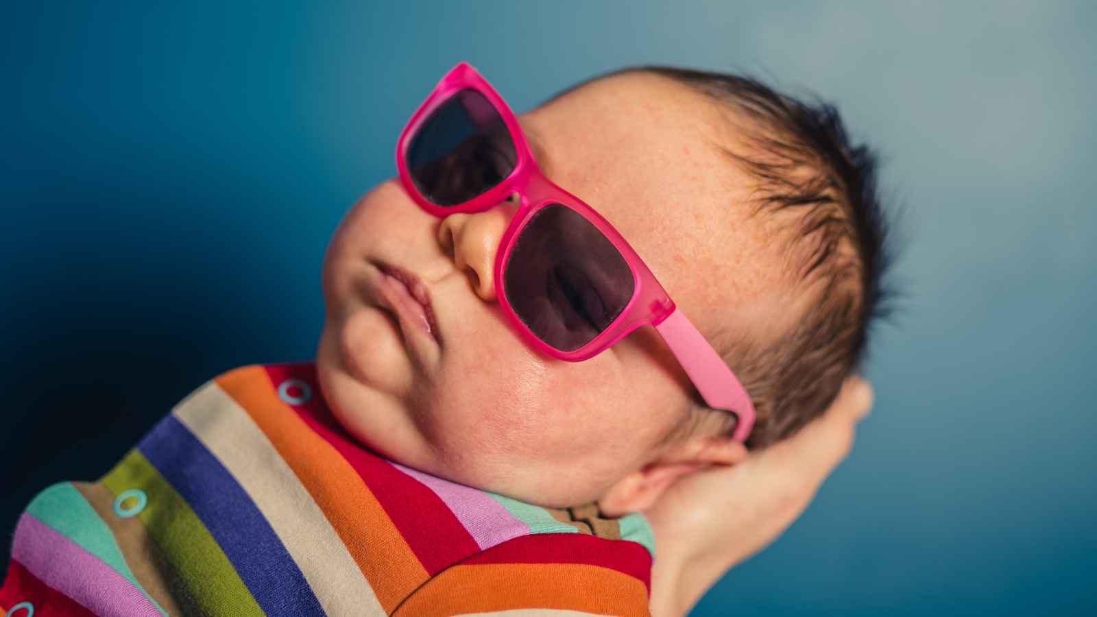 A baby wearing pink sunglasses and a colorful striped outfit.