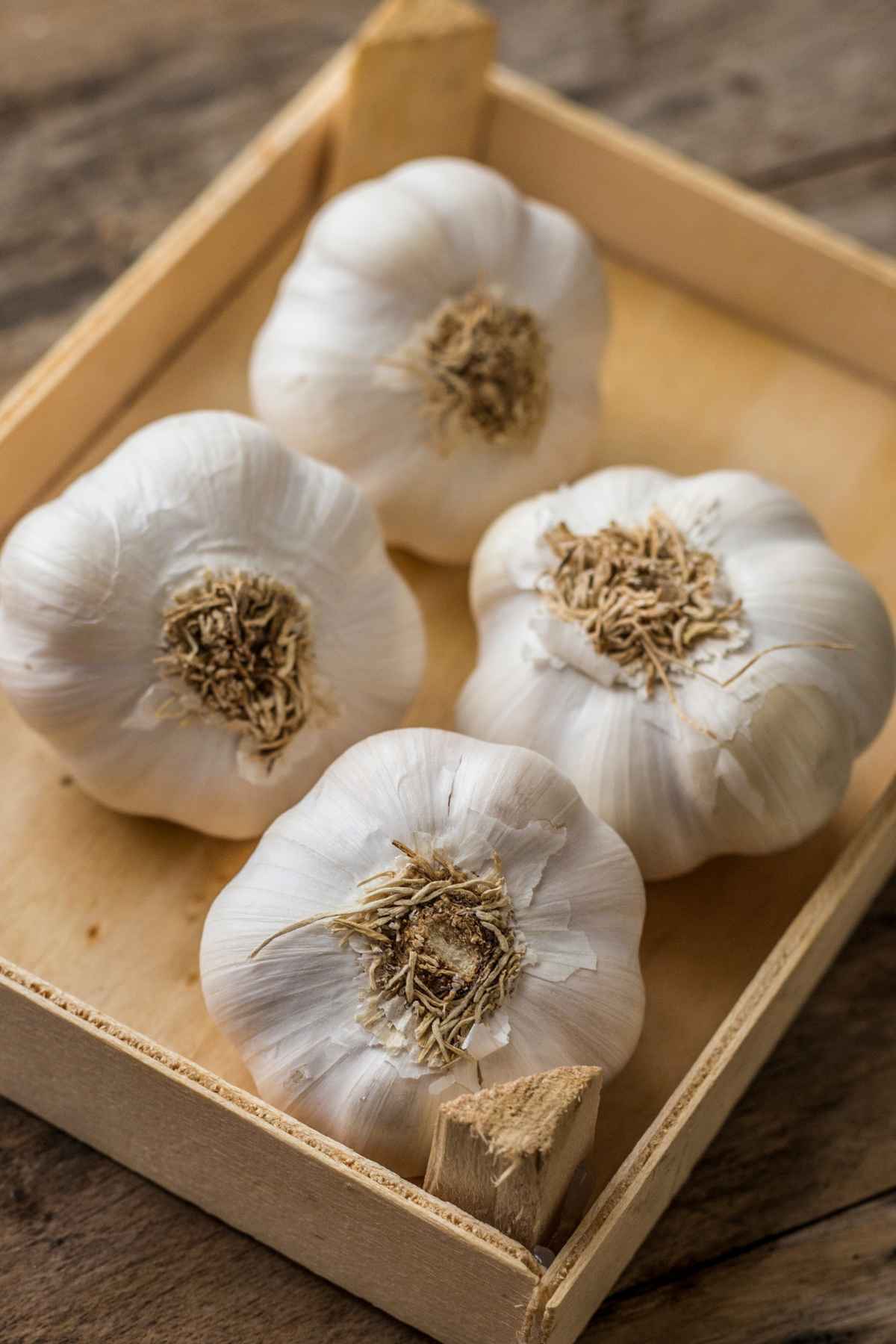 A wooden crate with four bulbs of garlic resting on a wooden surface.