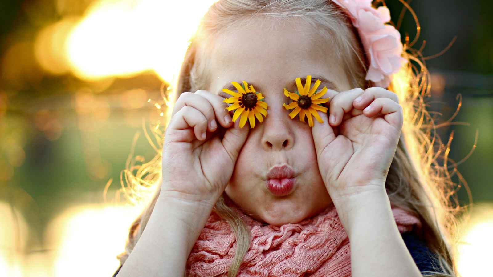 A young girl holds two yellow flowers over her eyes.