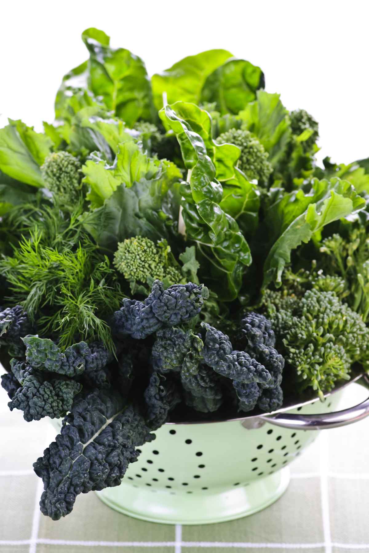 A colander filled with various fresh leafy greens.