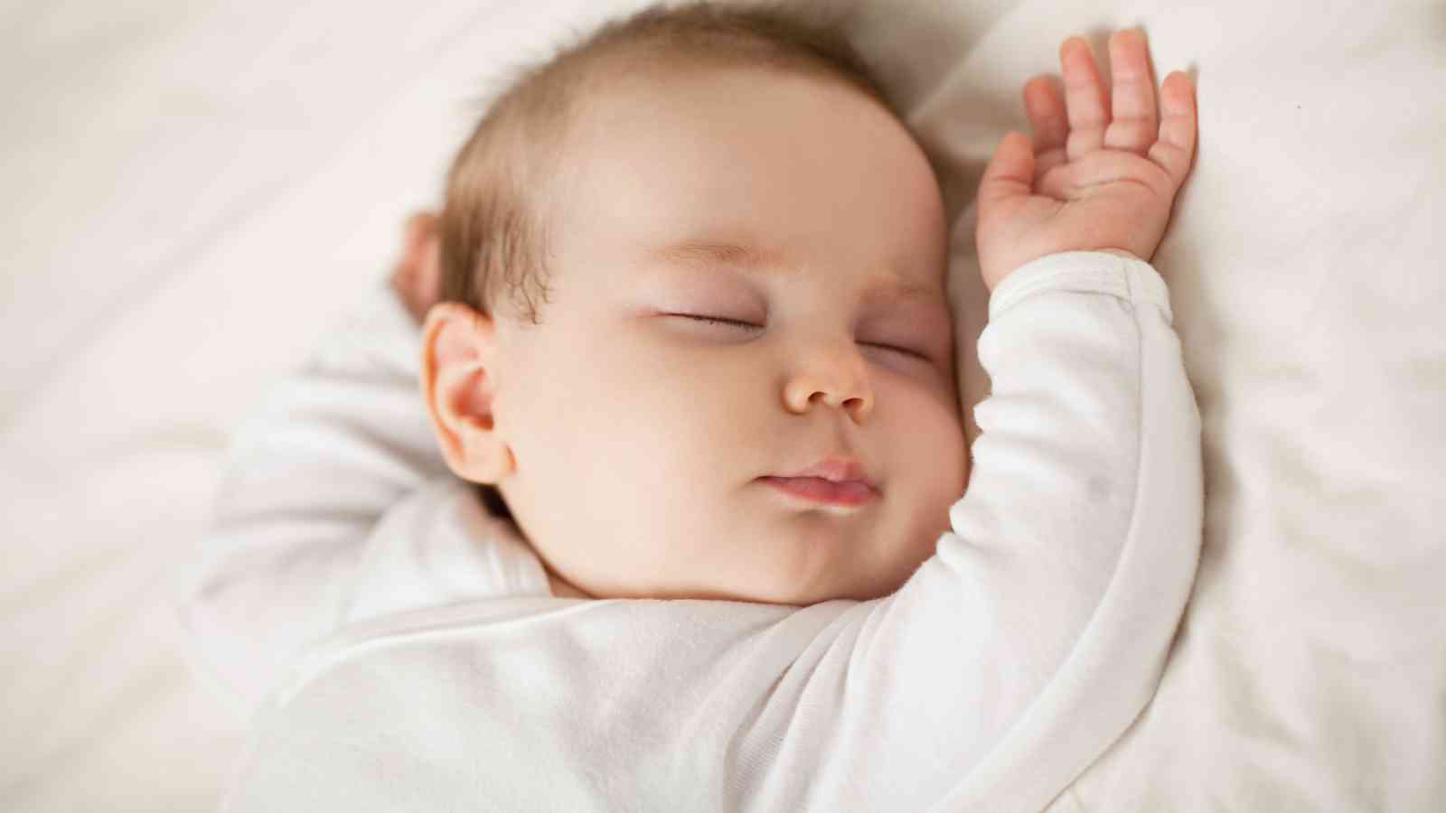 A baby in a white outfit is sleeping peacefully.