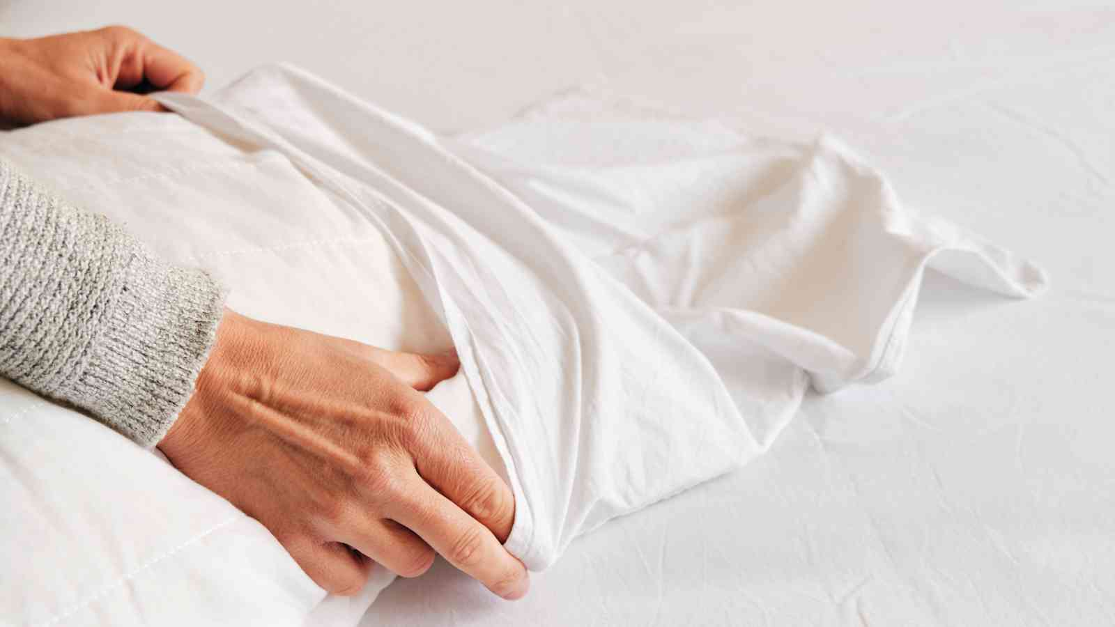 Hands putting a white pillowcase on a pillow.