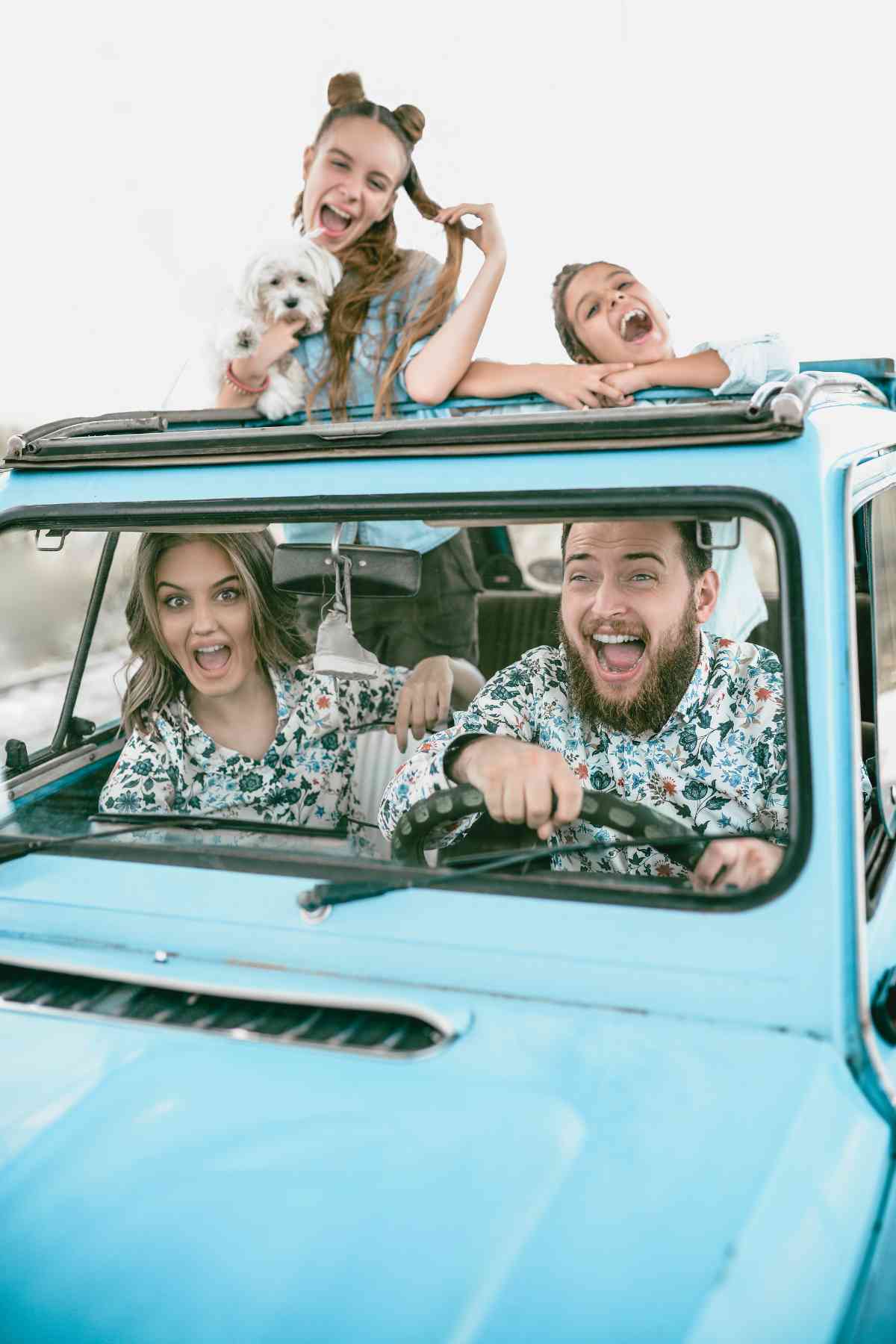 A family of four and a dog enjoy a ride in a blue convertible.