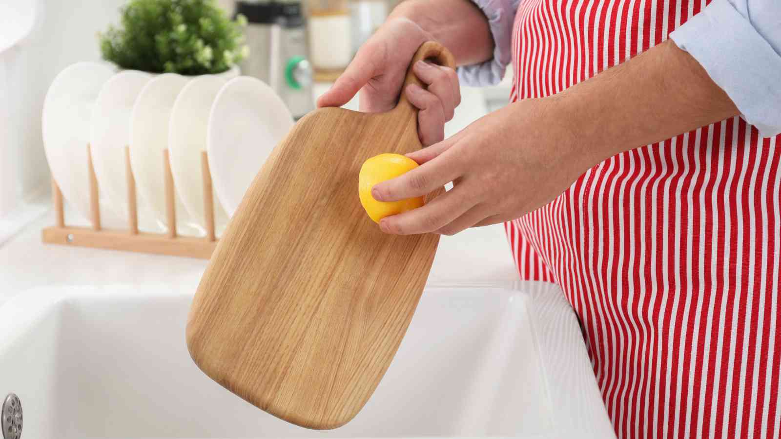 A person leaning a wooden cutting board with a lemon at a kitchen sink.