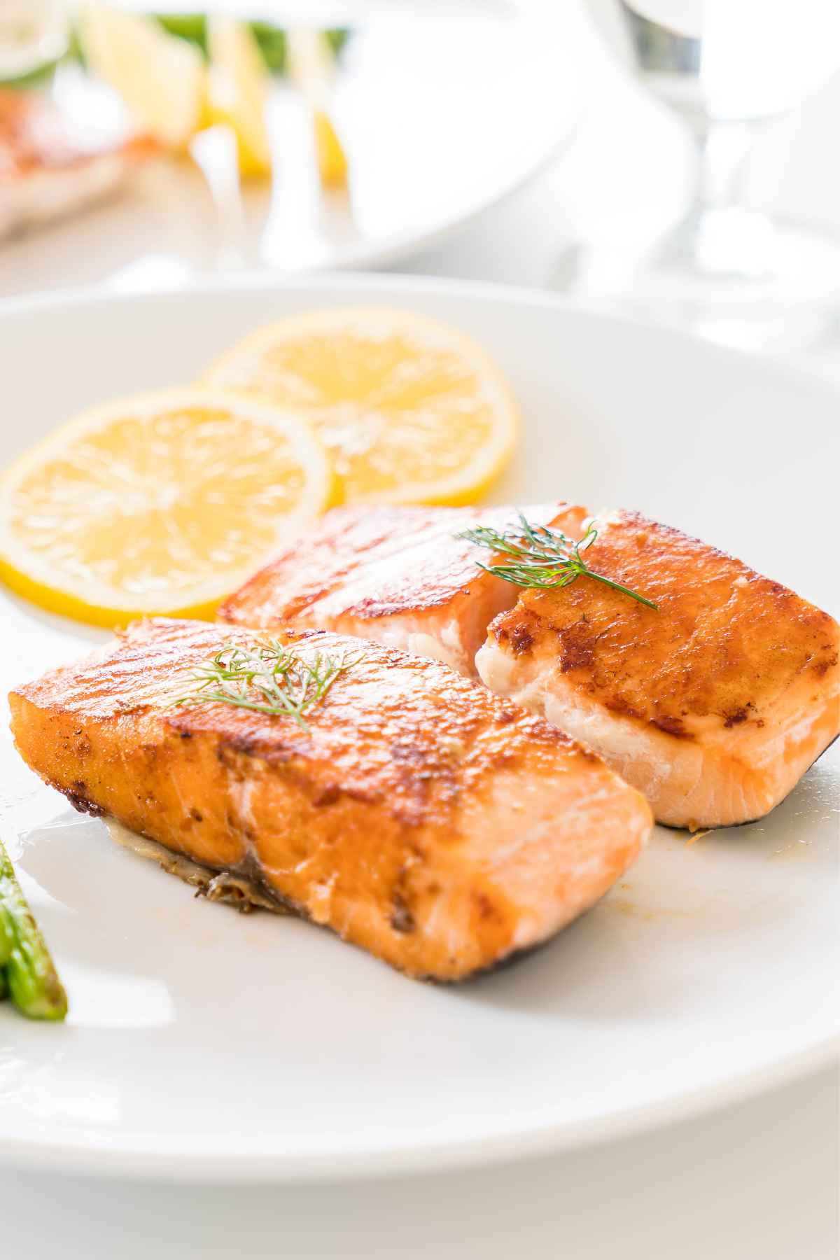 Two pieces of grilled salmon garnished with dill, accompanied by lemon slices, served on a white plate.