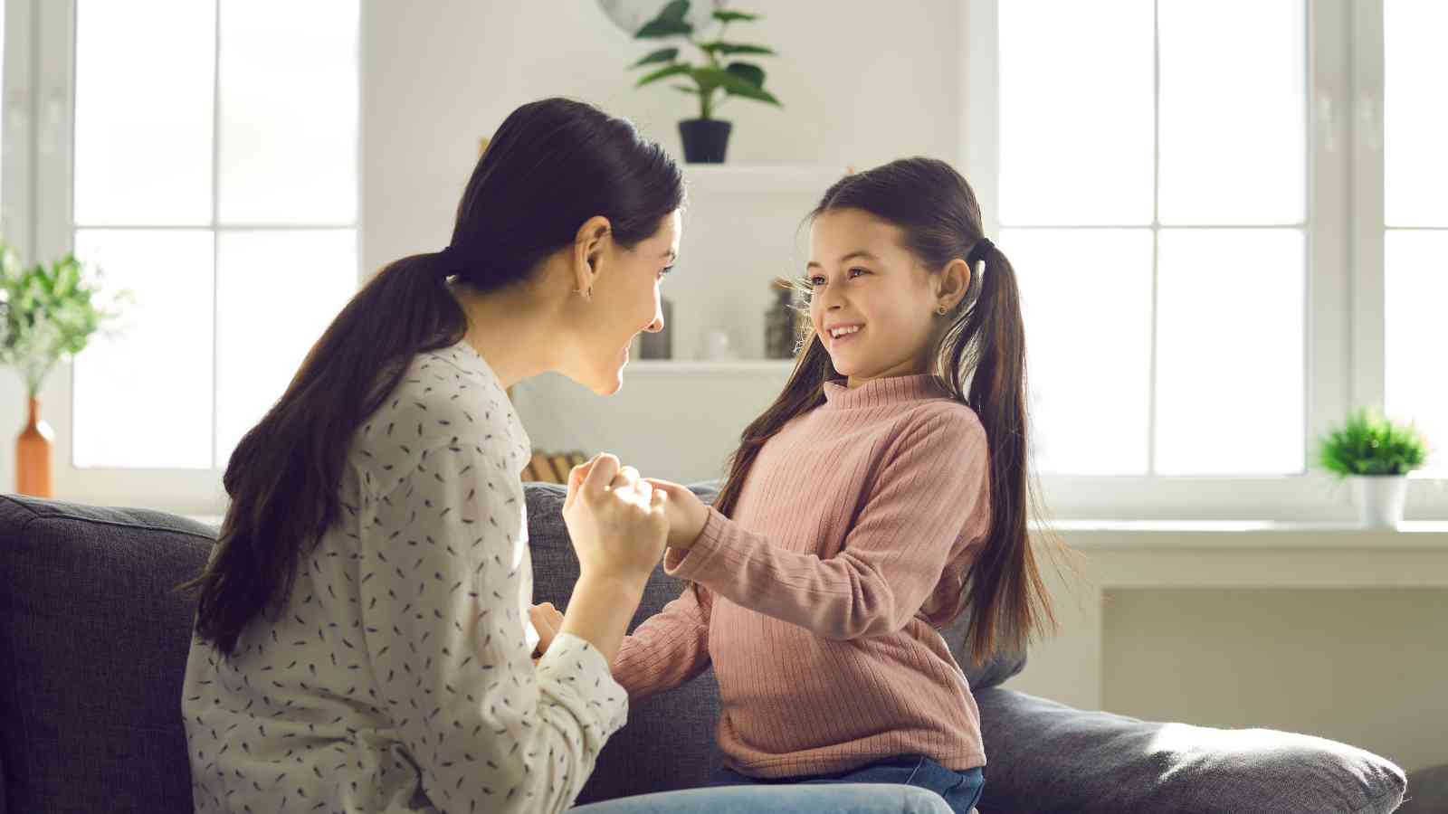 A mom and he daughter holding hands and smiling at each other.