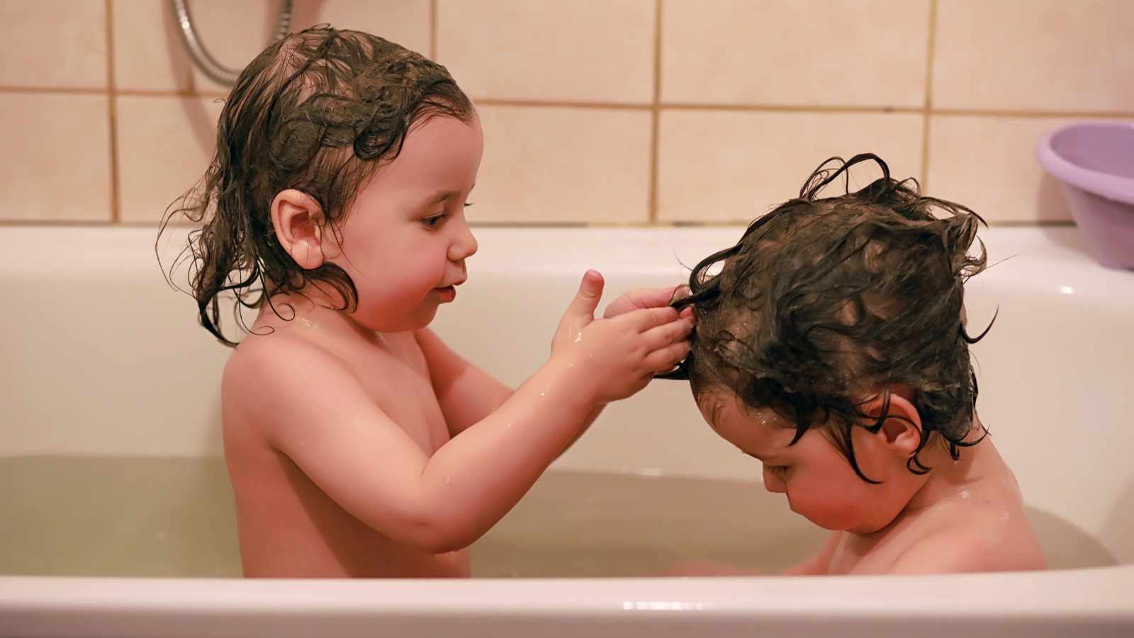 Two young children with wet hair are sitting in a bathtub