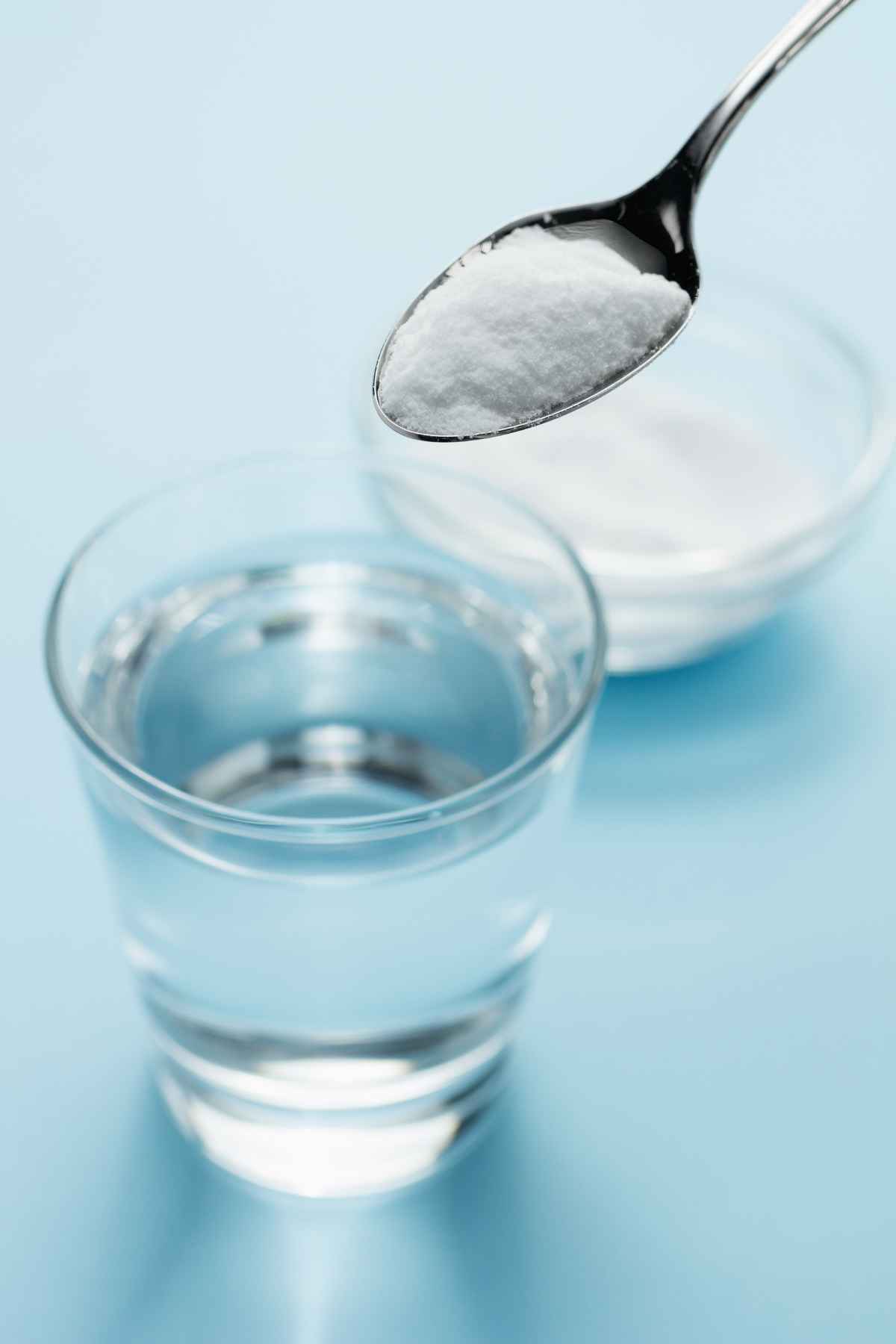 A spoonful of baking soda is held above a glass of clear water.