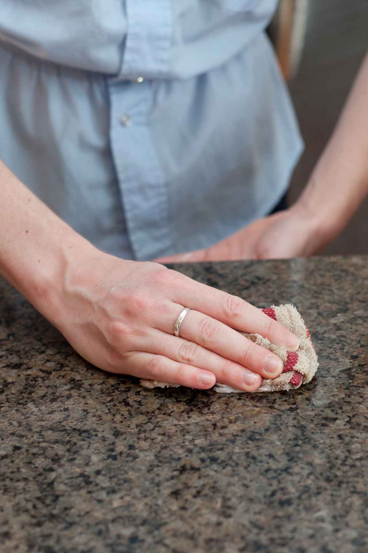 A person wearing a blue shirt is wiping a countertop with a cloth.