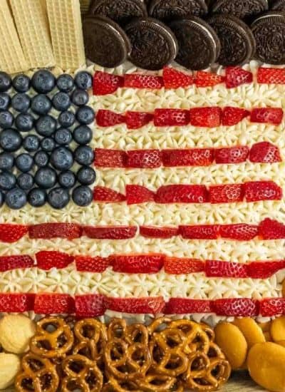 A 4th of July dessert board with an American flag design made from berries and white frosting surrounded by assorted snacks.