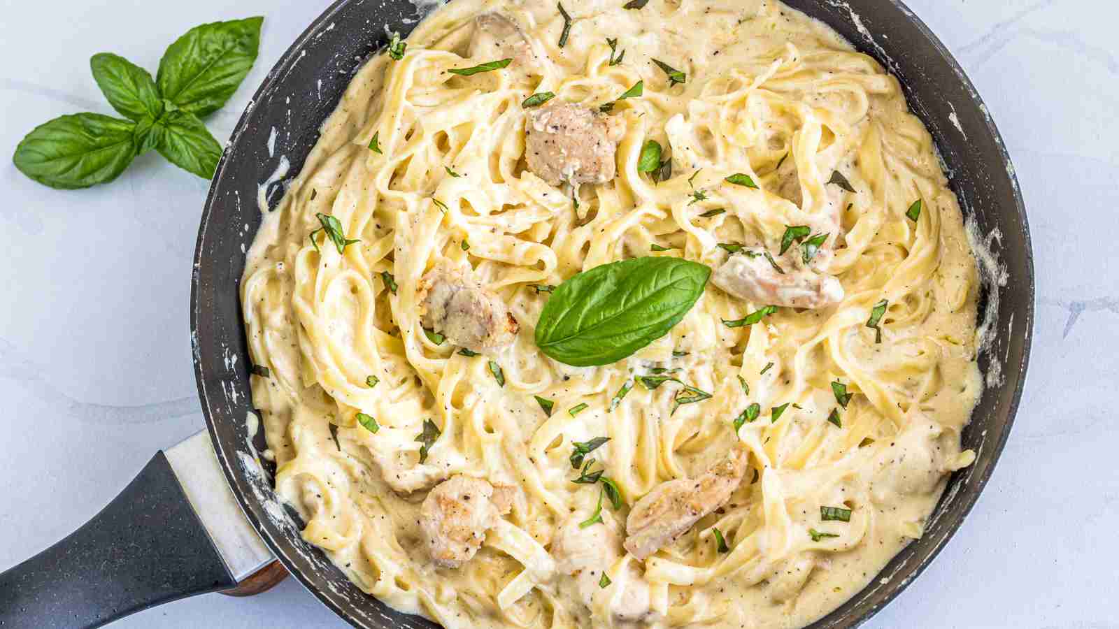 A skillet filled with alfredo pasta topped with an herb in the middle.