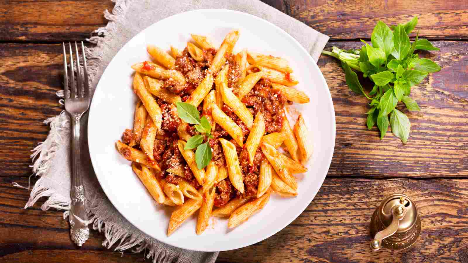 A plate of bolognese pasta on a wooden surface.