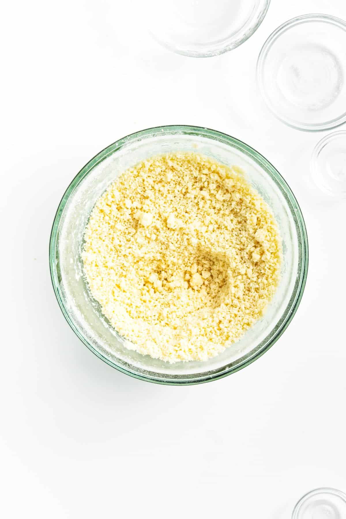 A glass bowl containing a crumbly mixture of flour and butter, viewed from above.