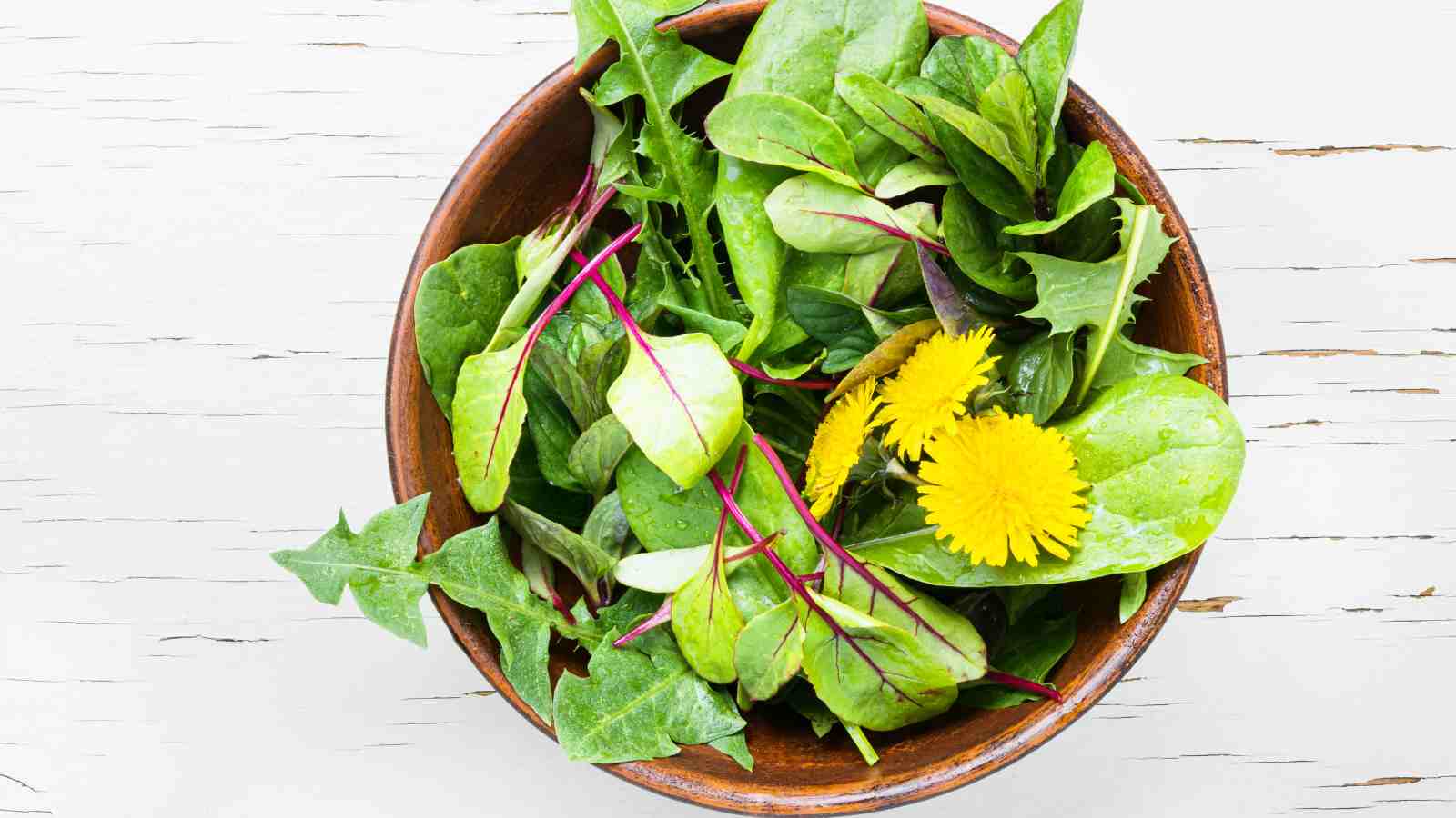 A wooden bowl filled with dandelion greens salad.