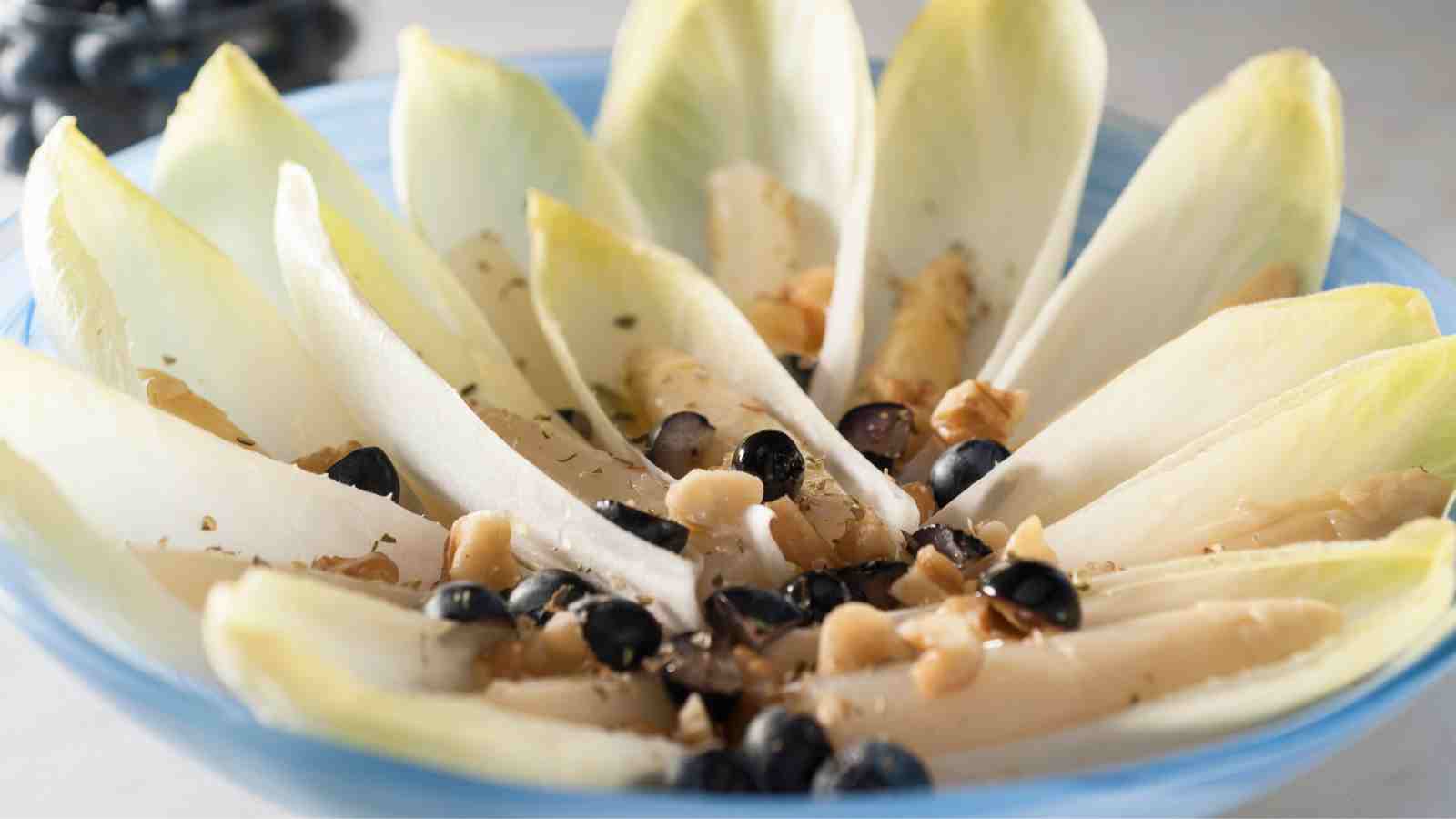 A close-up of a salad with endive leaves, blueberries, walnuts, and a light sprinkle of herbs, arranged in a blue bowl.