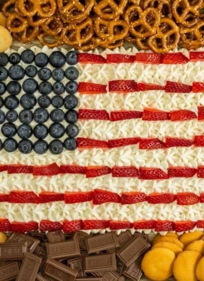 A 4th of July dessert board with an American flag design made from berries and white frosting surrounded by assorted snacks.