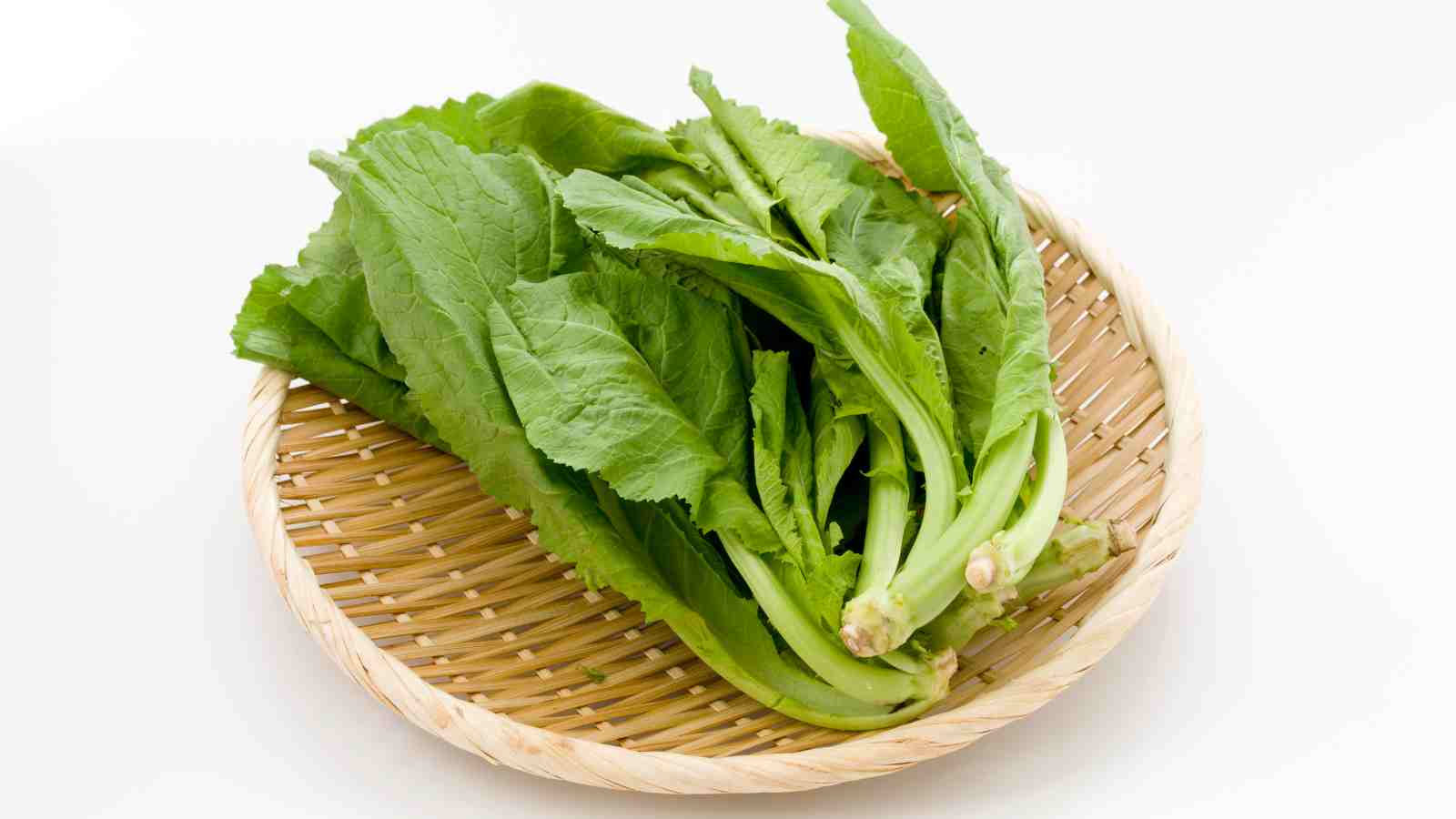 A bamboo basket holding fresh mustard green vegetables on a white background.