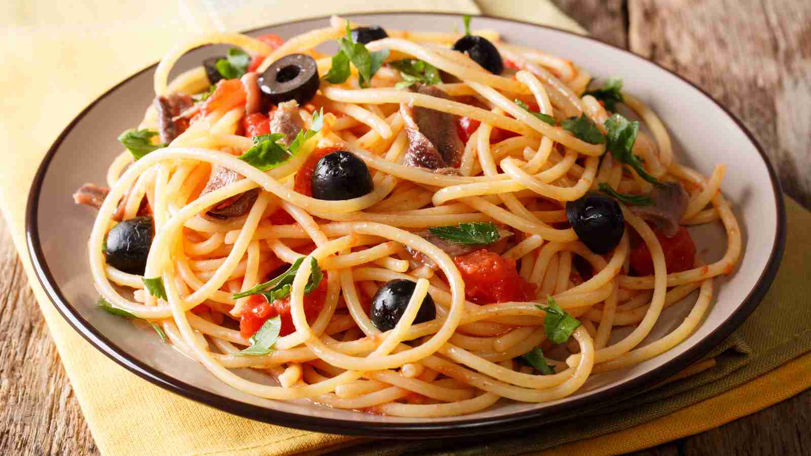 A plate of putanesca pasta topped with sliced black olives.