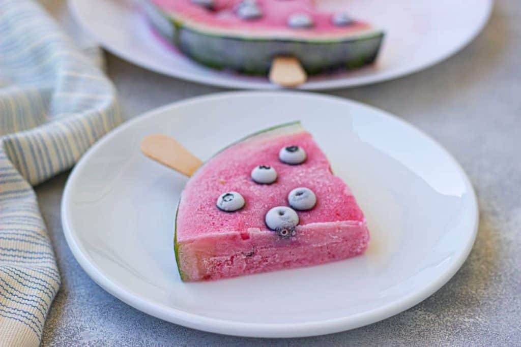 A slice of watermelon frozen yogurt on a white plate with blueberries.