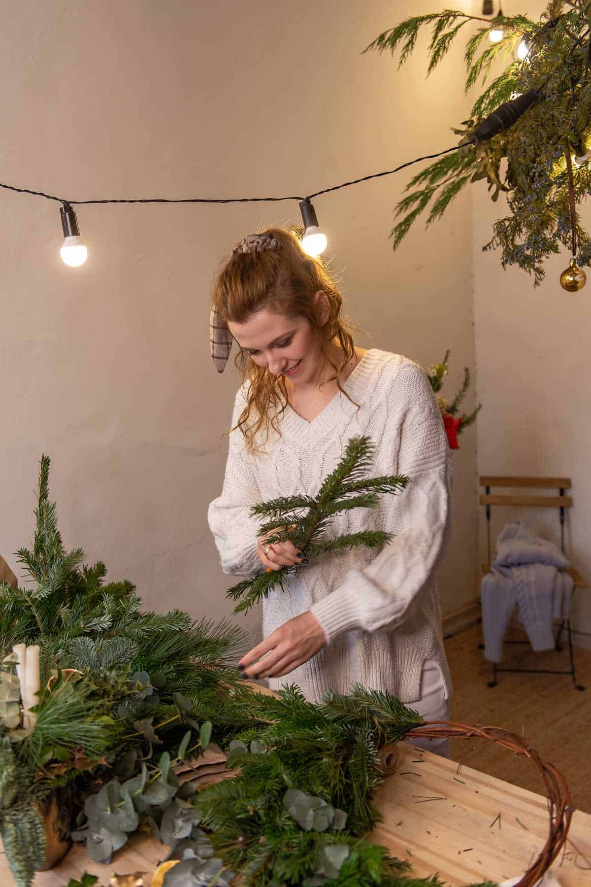 A person in a white sweater making a handmade Christmas wreath.