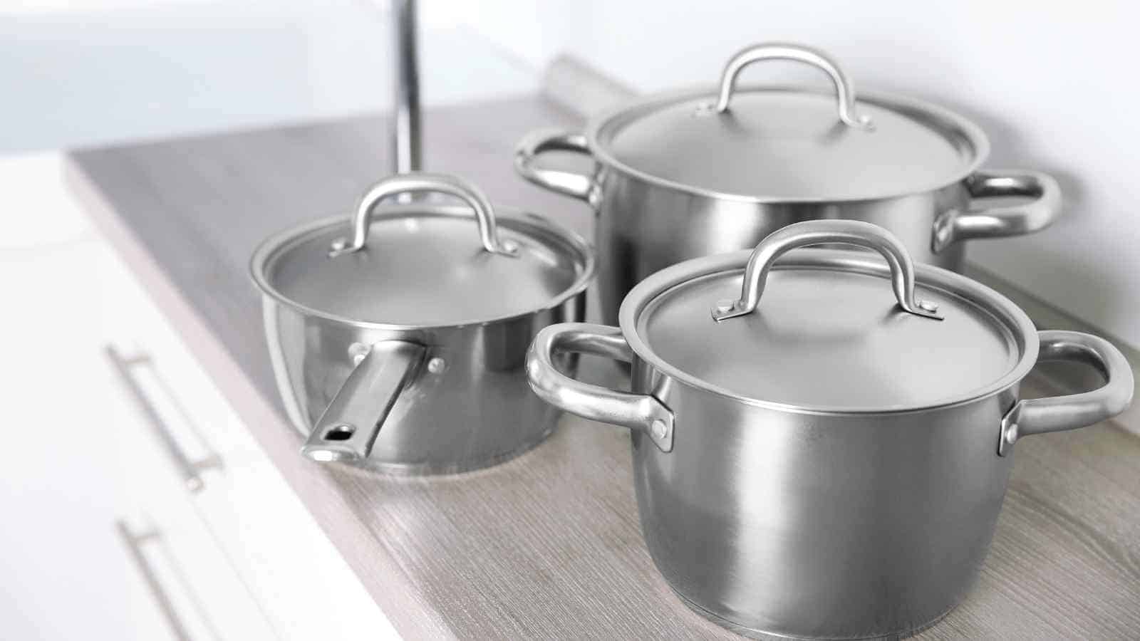 Three aluminum pots of varying sizes with lids are placed on a kitchen countertop.