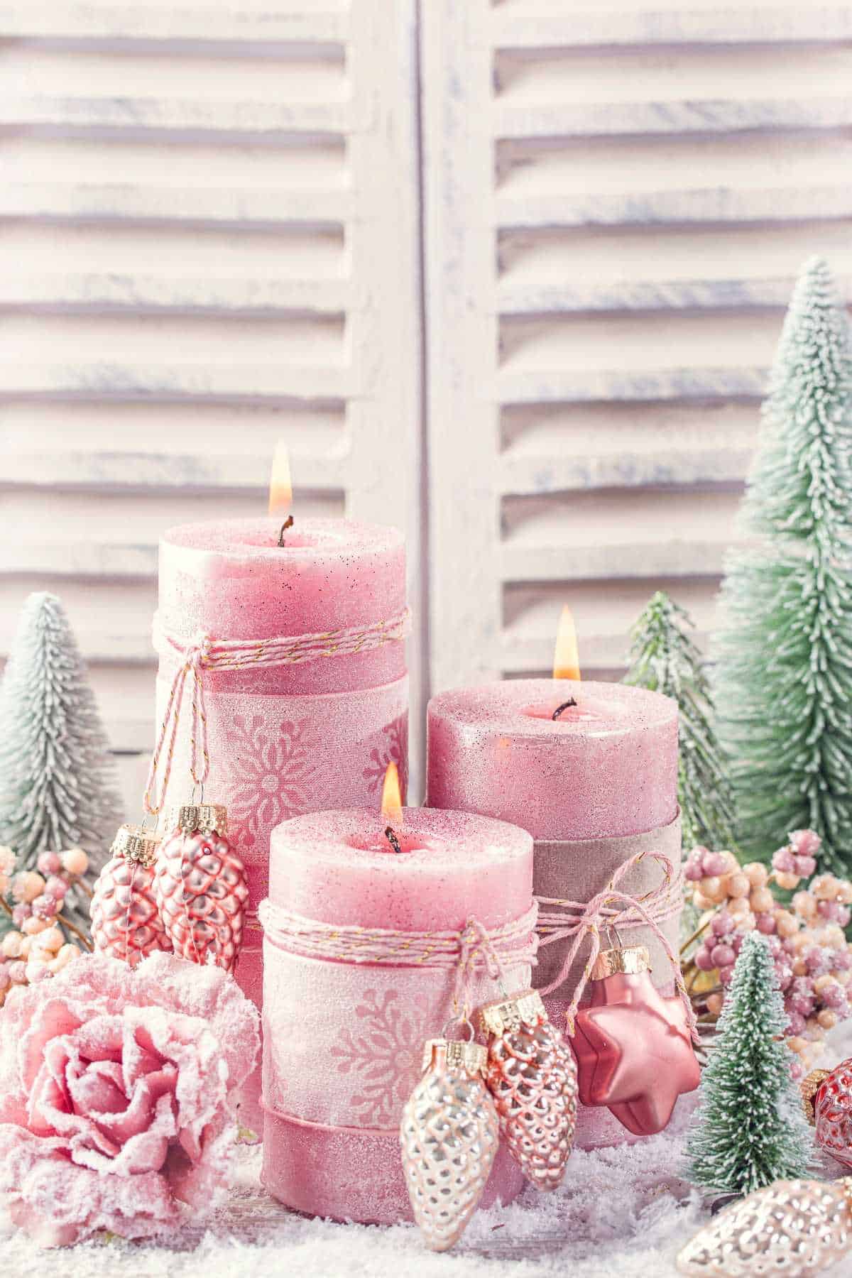 Three pink candles of varying heights, decorated with small pinecone ornaments.