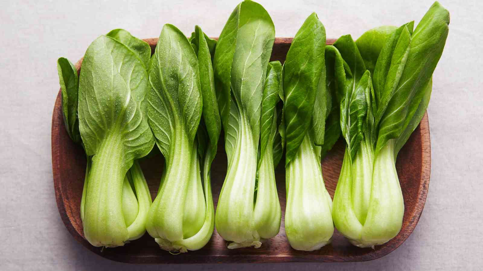Five fresh bok choy heads arranged in a row on a wooden tray.