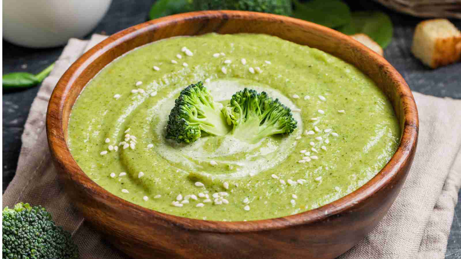 A wooden bowl filled with green broccoli soup.