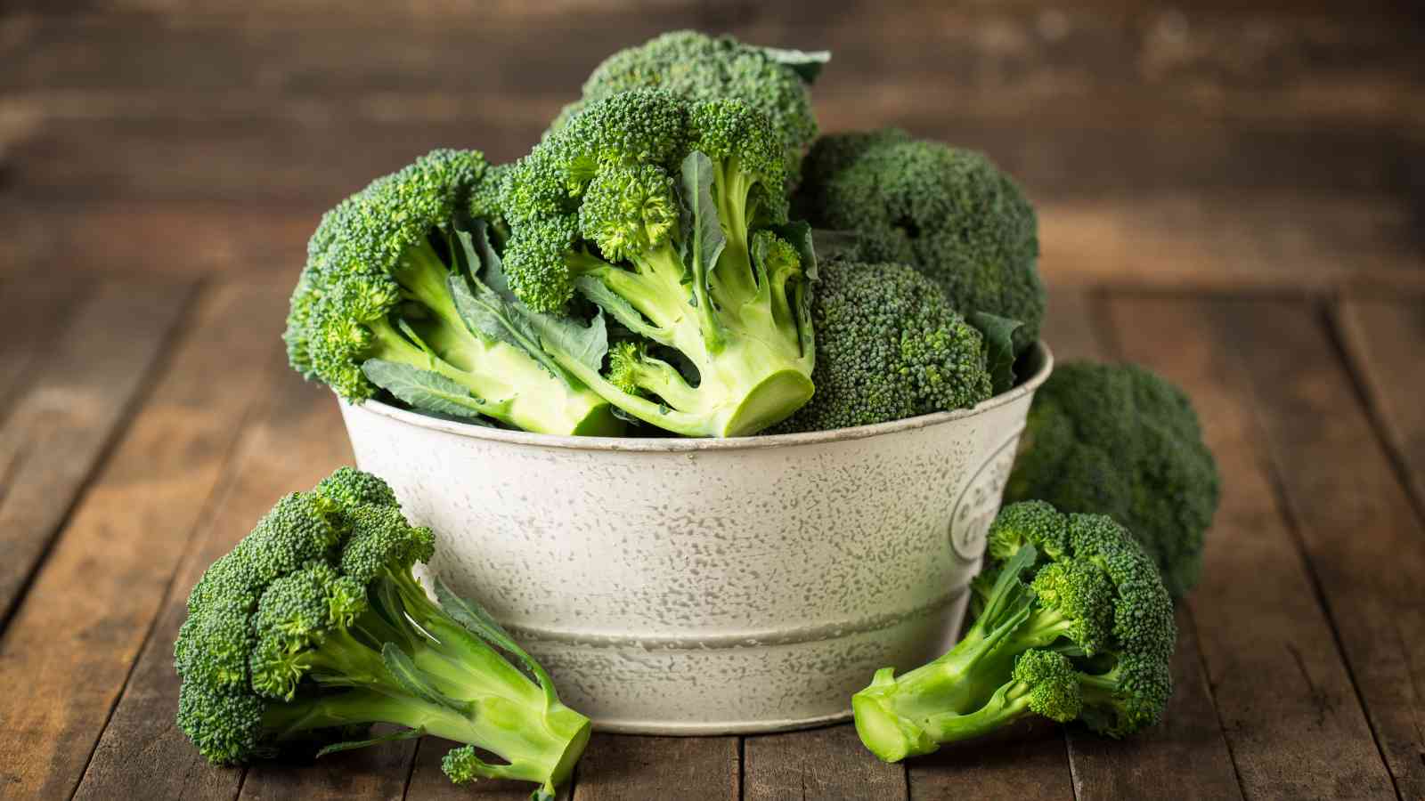 A white bowl filled with fresh broccoli florets on a wooden surface.