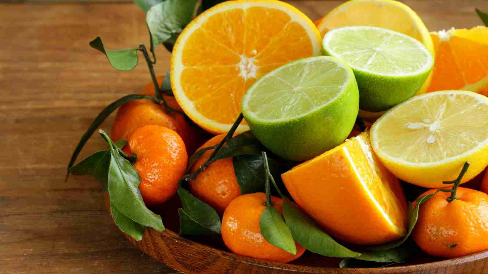 A wooden bowl filled with fresh citrus fruits.