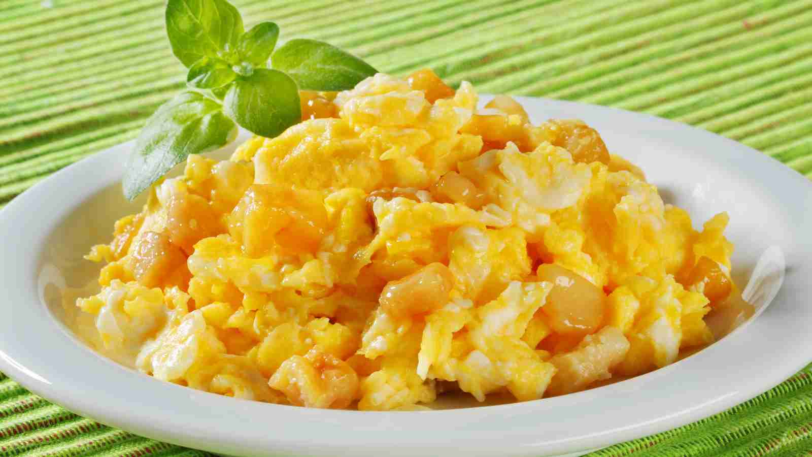 A plate of scrambled eggs garnished with a sprig of fresh basil, set on a green textured placemat.