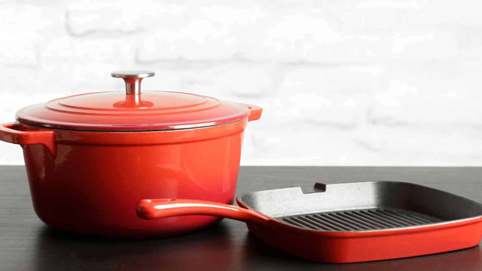 A red enamel pot and grill pan placed on a black surface, against a white brick wall background.